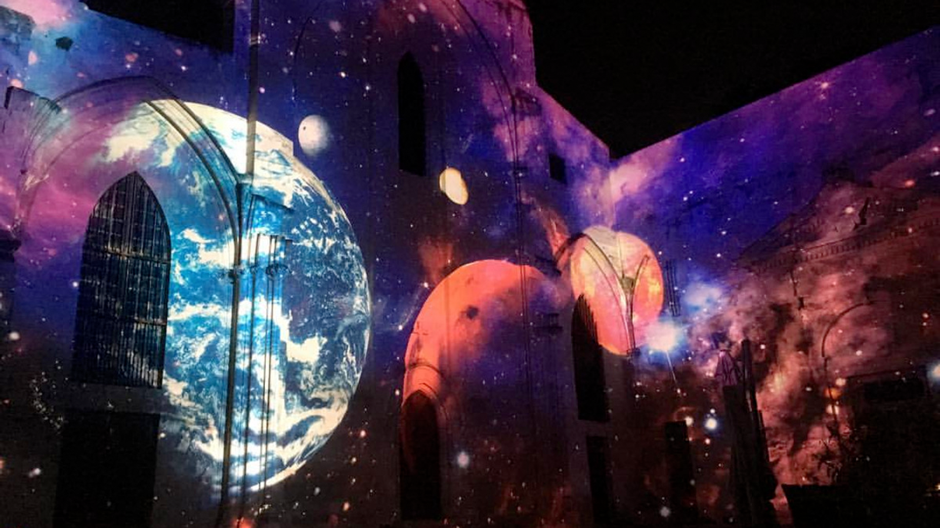 Planets and a purple-blue galaxy projected onto the Célestins church during Festival Hélios 2018 in Avignon.