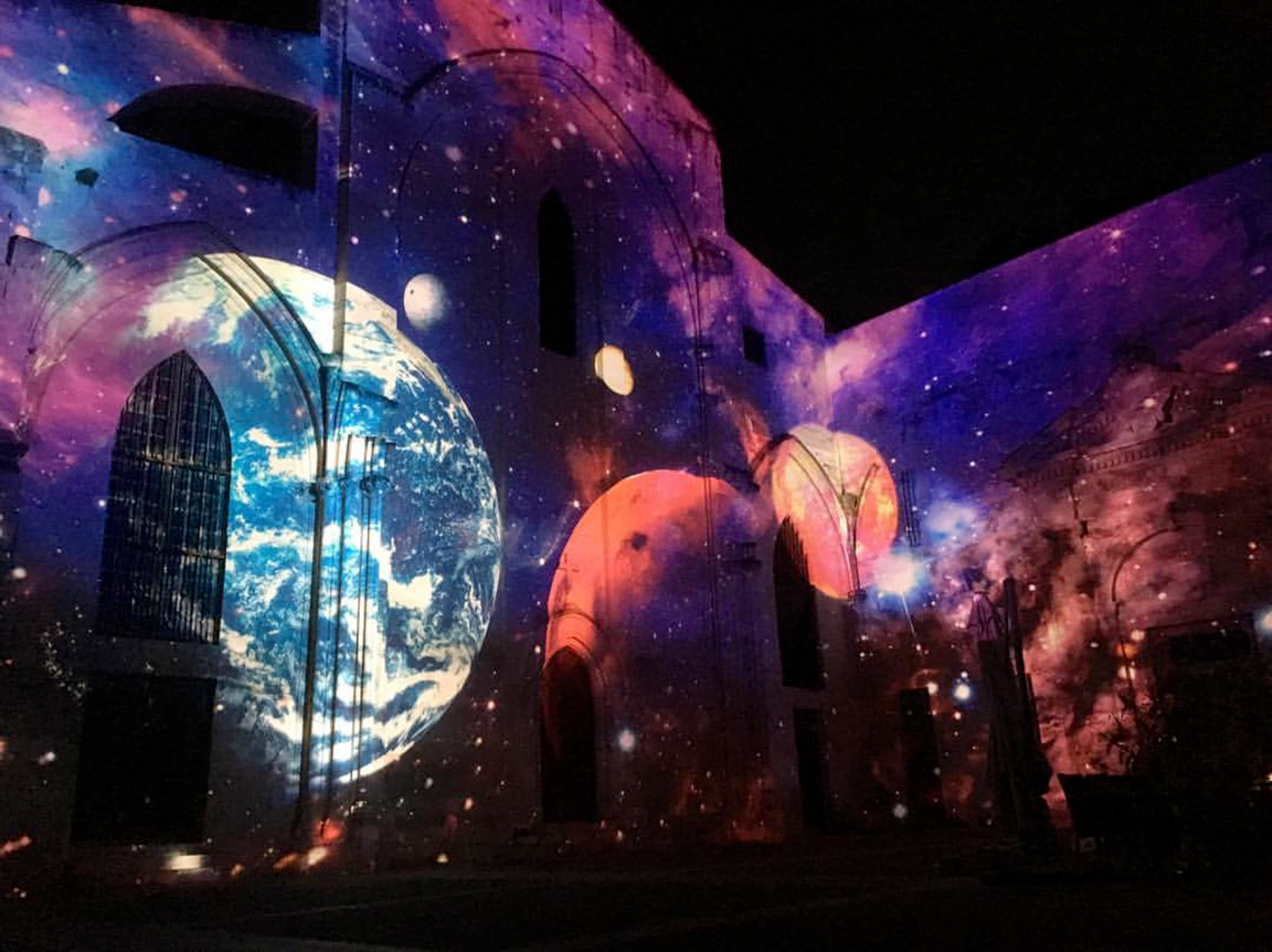 Planets and a purple-blue galaxy projected onto the Célestins church during Festival Hélios 2018 in Avignon.