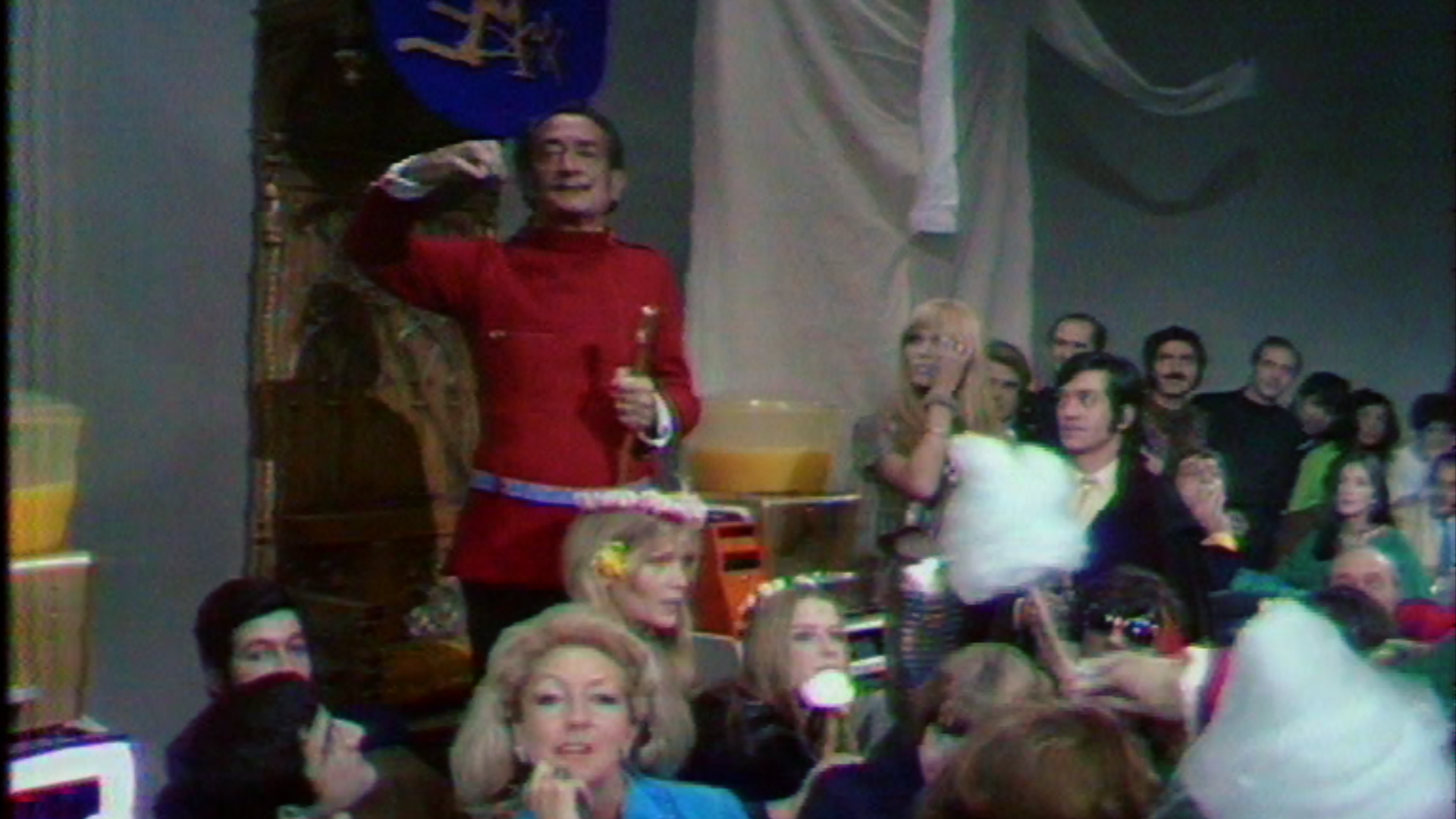Archive television scene with a man in red standing above a seated audience.