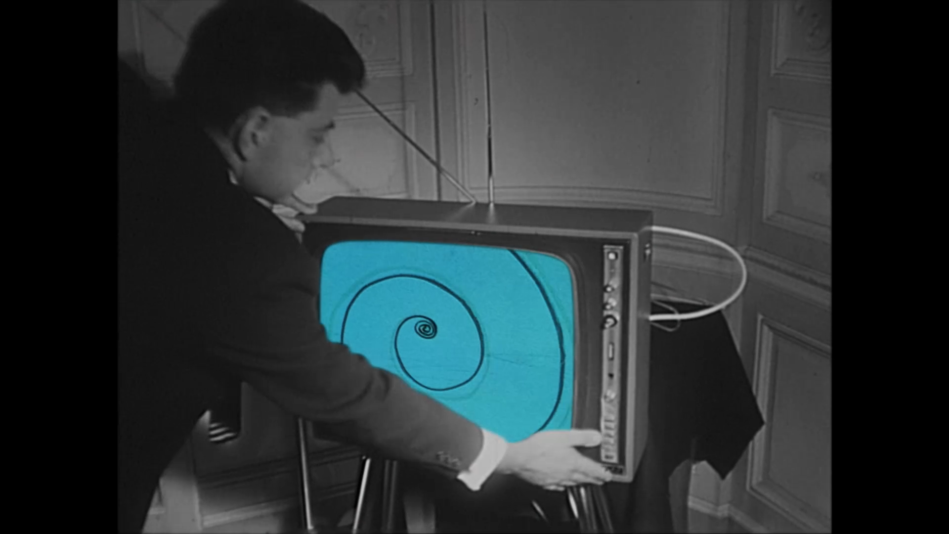 Black-and-white archive image of a man tuning a television with a cyan spiral on its screen.