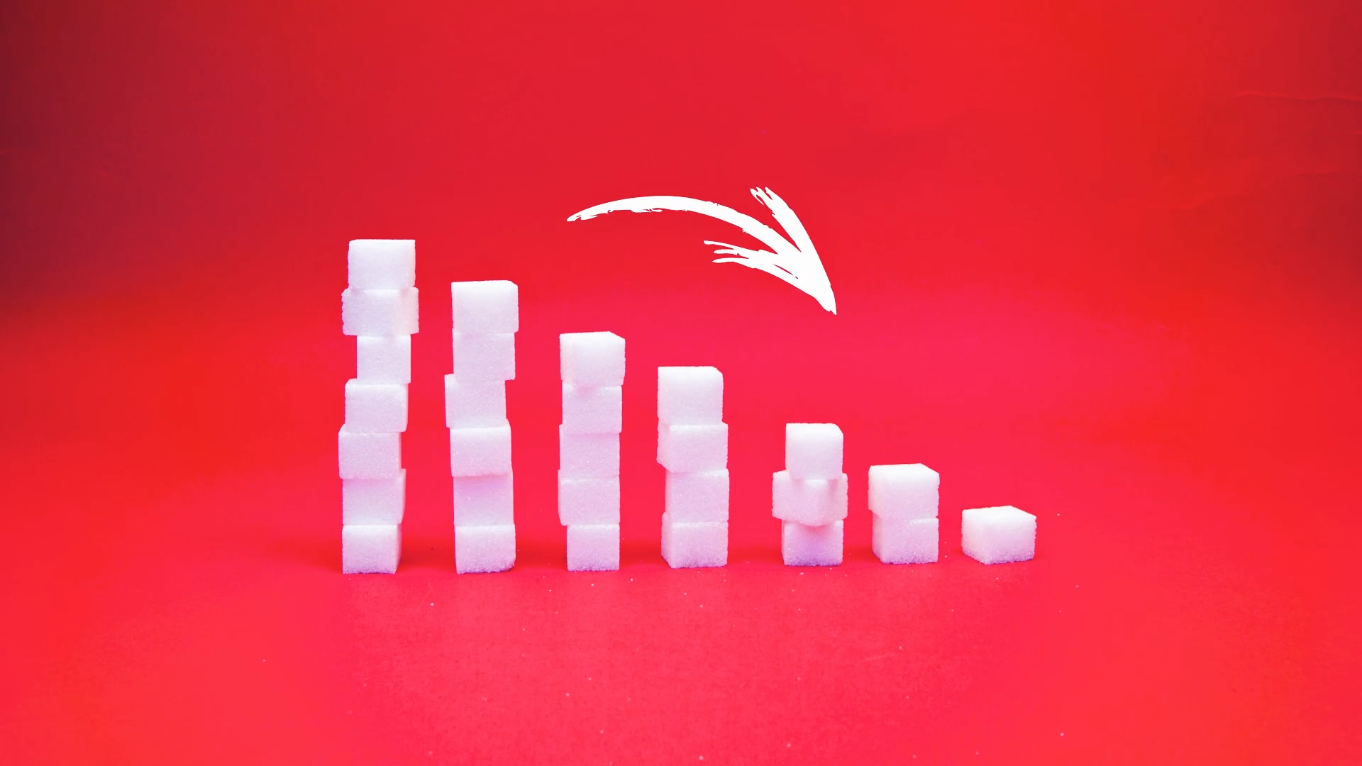 Descending stacks of sugar cubes on a red background with a hand-drawn white arrow.