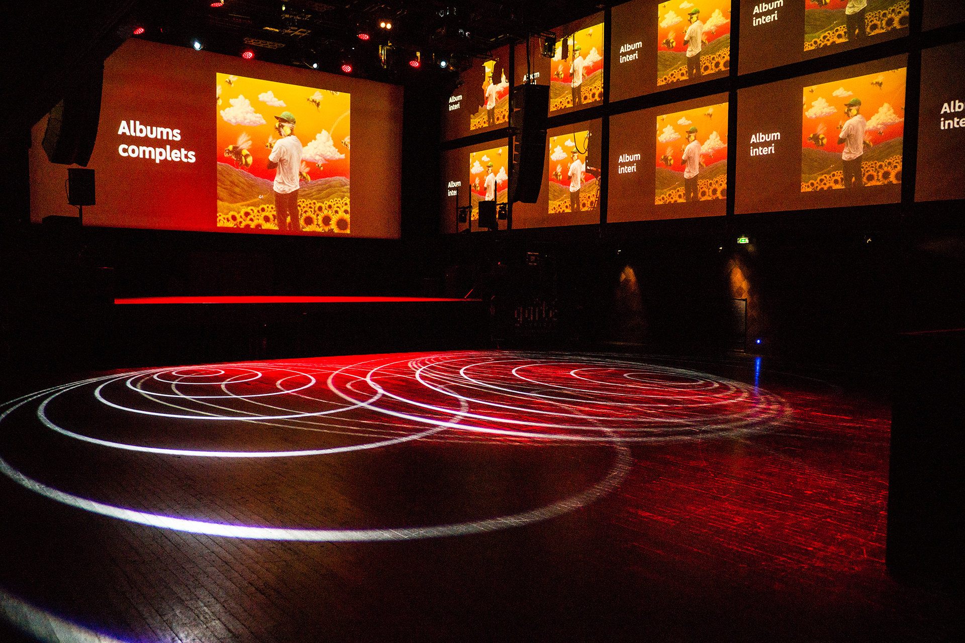 Album artwork and multilingual messages across the stage and side screens.